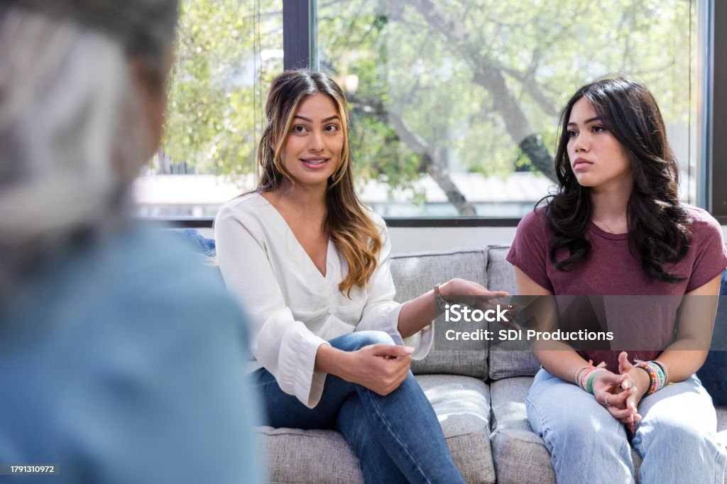 A parent and teenager sitting together on a couch talking with a counselor